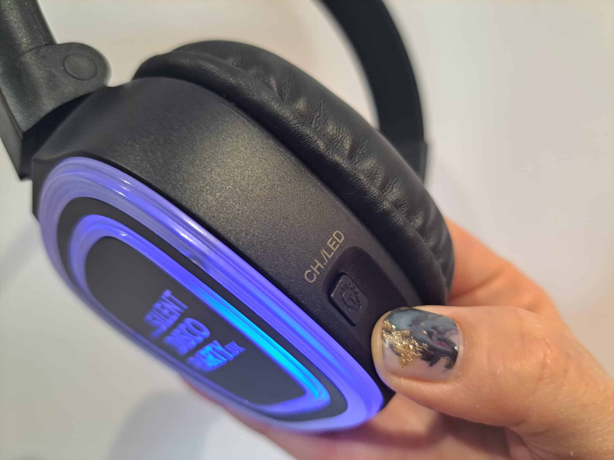 Close up of a Silent Disco Party UK wireless headphone glowing blue held in hand showing the padded ear cup and CH LED channel button